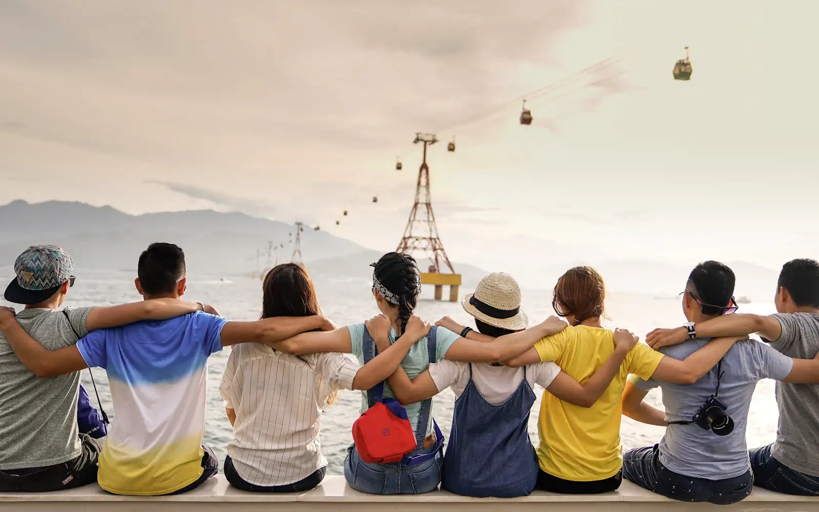 Friends travelling together, arms around each other's shoulders, looking out over a bay