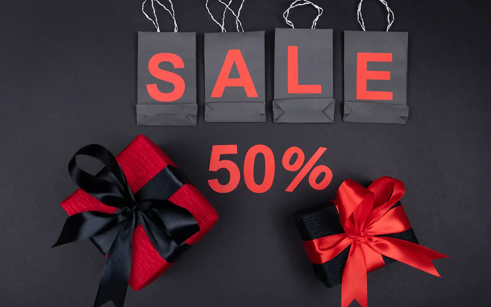 Black shopping bags spelling SALE in red letters, a 50% sign and two gift boxes tied with ribbon