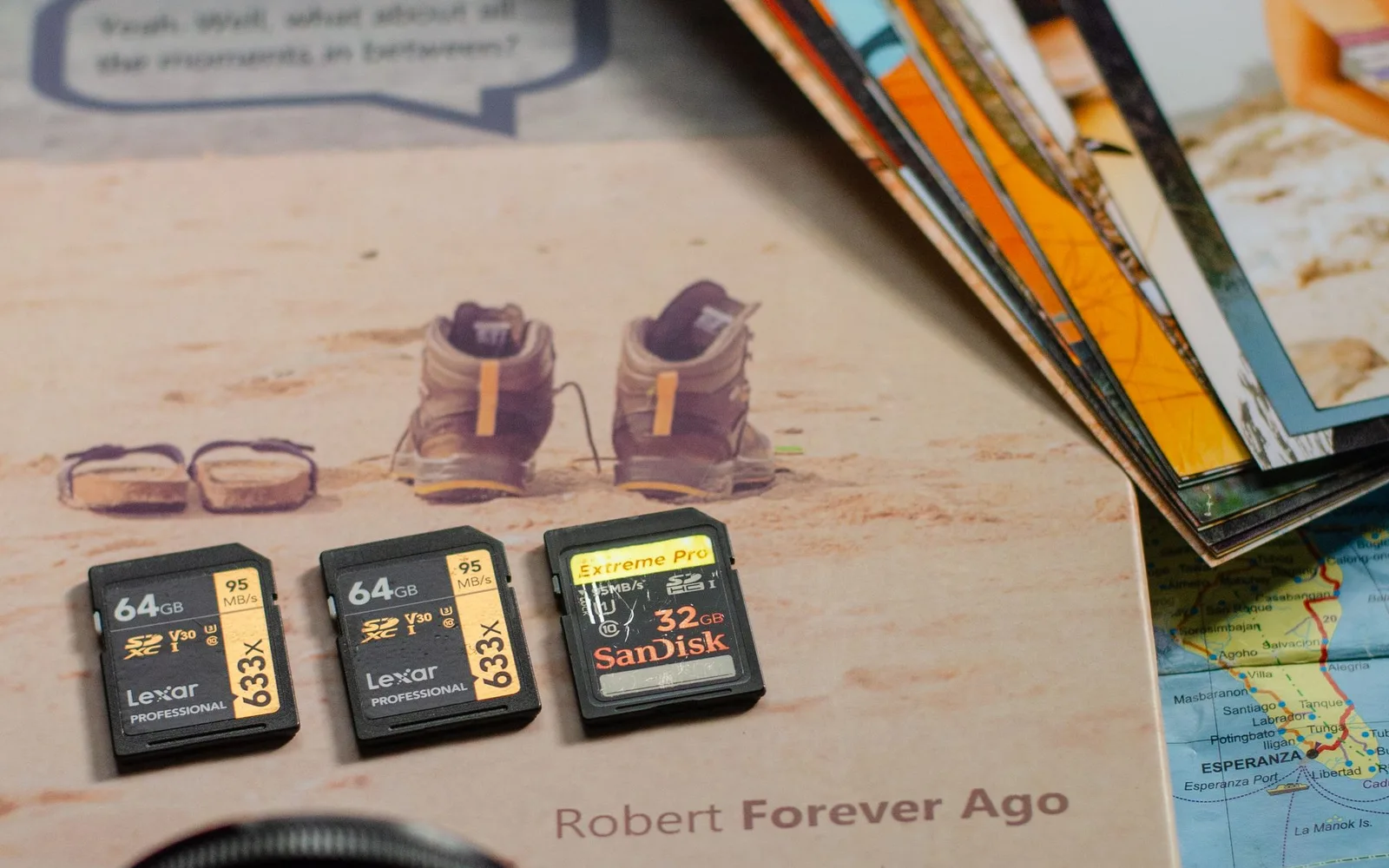 Camera memory cards beside printed photographs and a lens on an open book