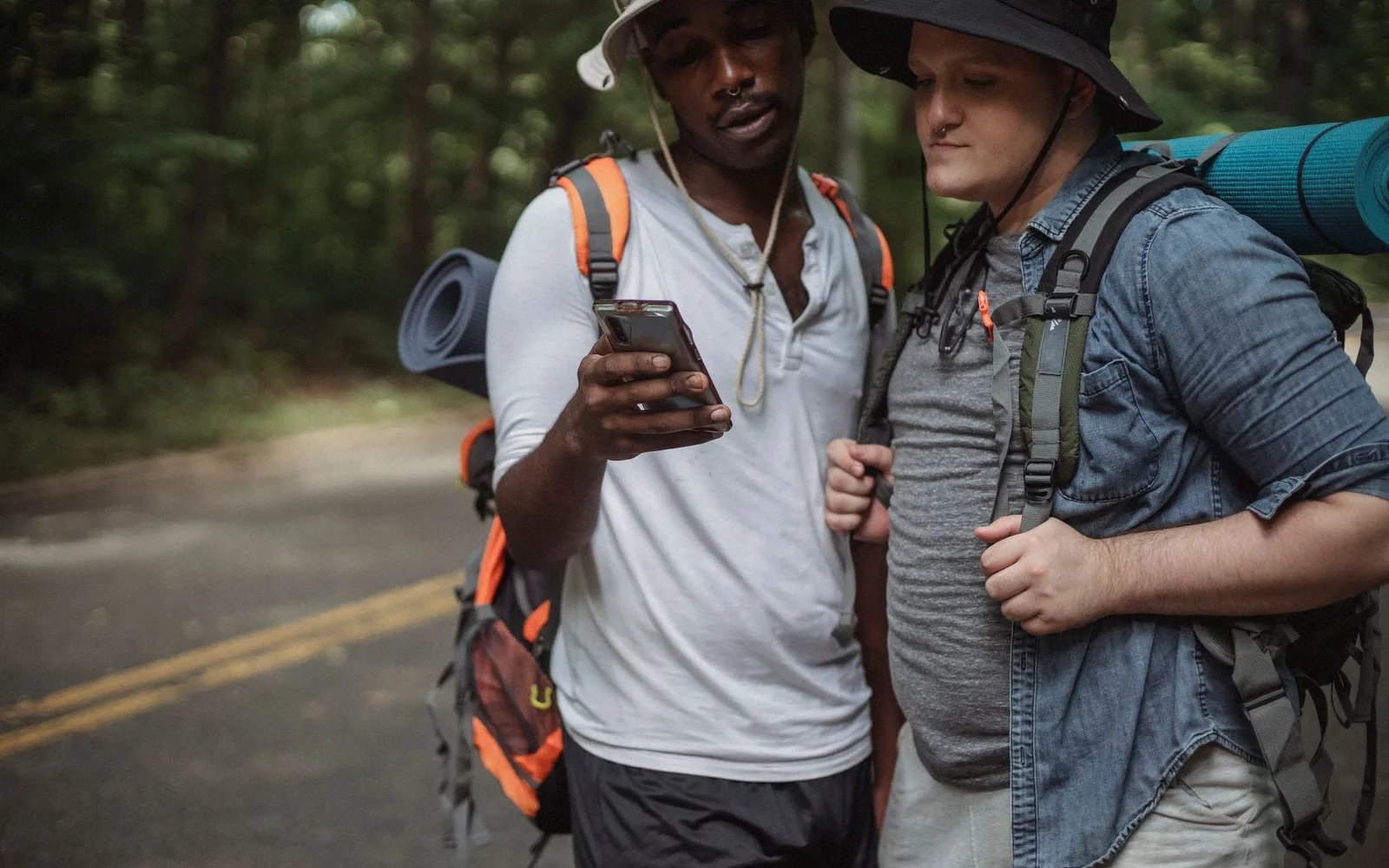 Two hikers looking together at a smartphone beside a forest road