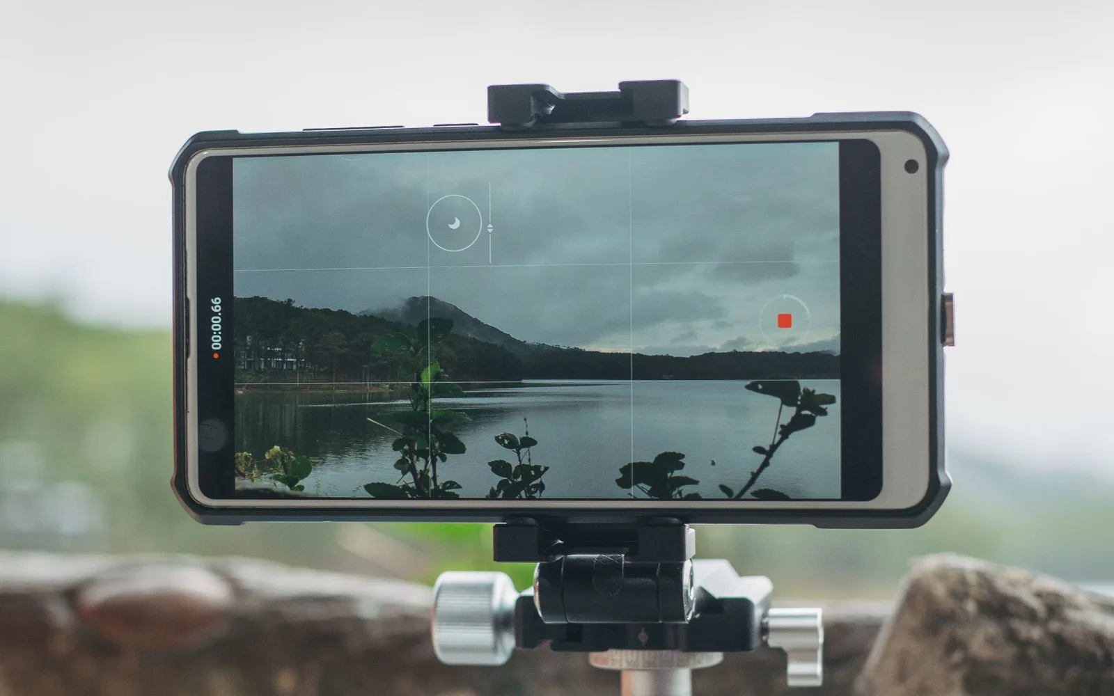 A smartphone mounted horizontally on a tripod, framing a landscape across water