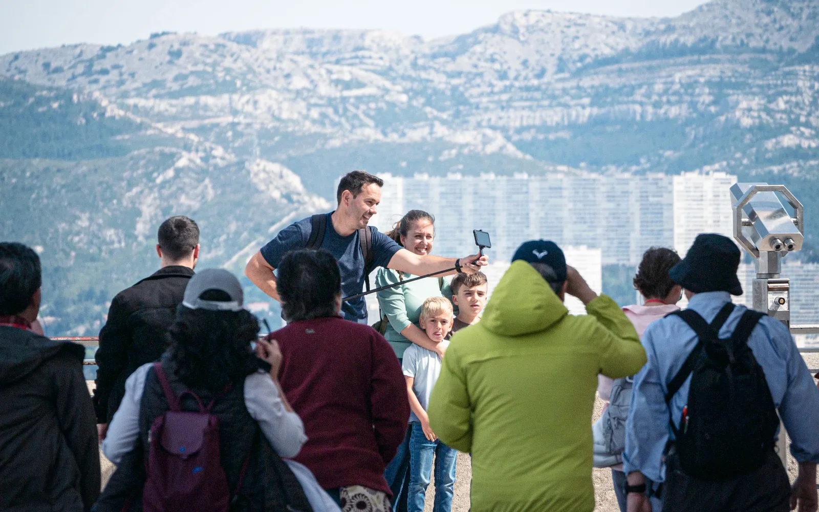 Travelers posing for a photograph at a busy mountain viewpoint