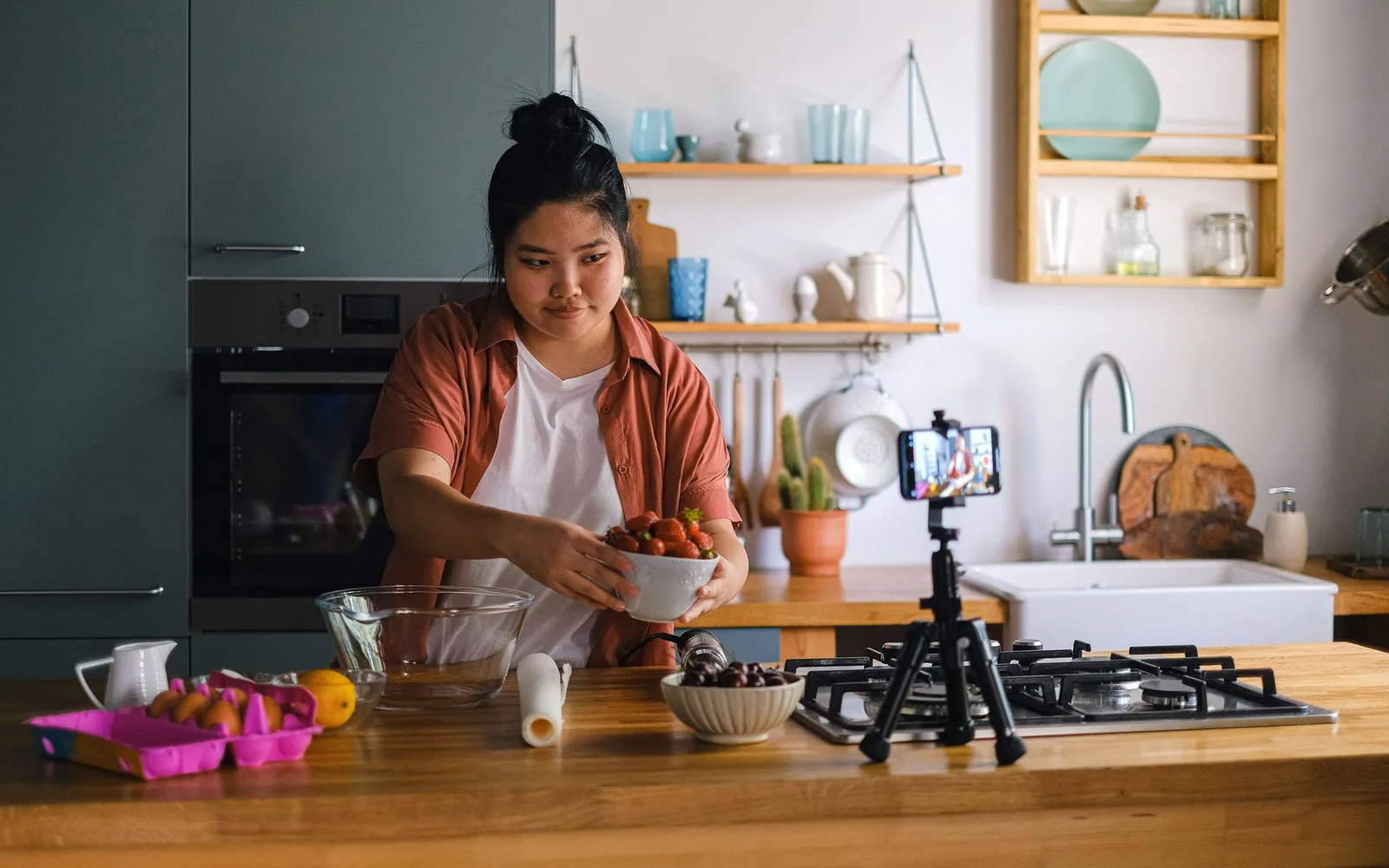 A woman preparing fruit while a smartphone on a tripod records the kitchen counter